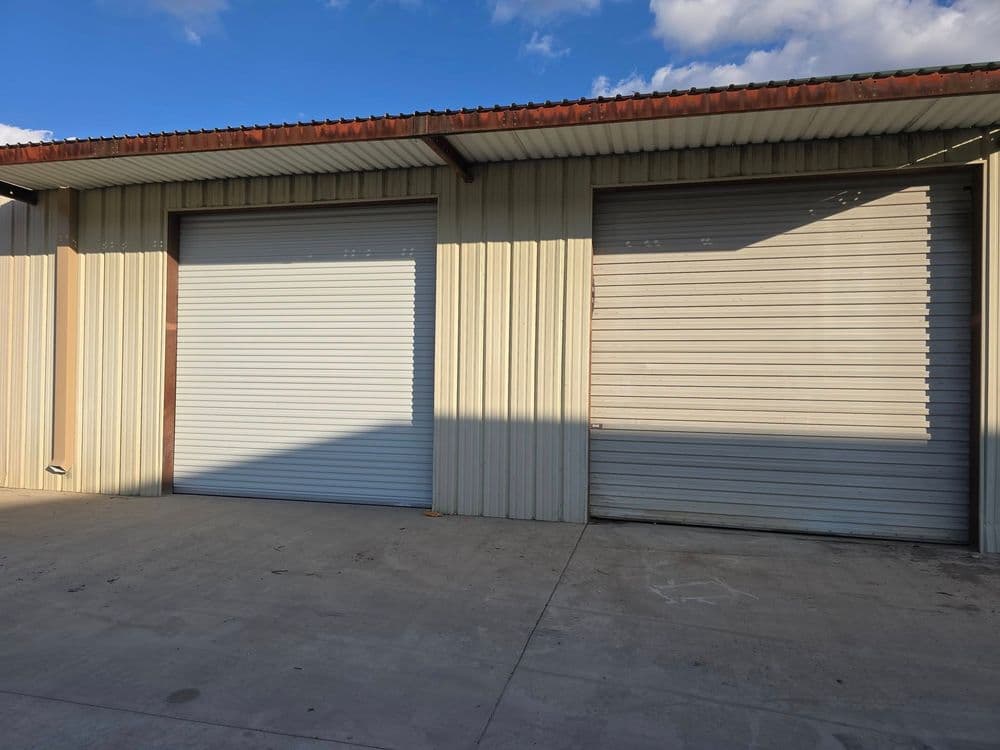 Two metal garage doors on a storage unit building with clear blue sky in the background.