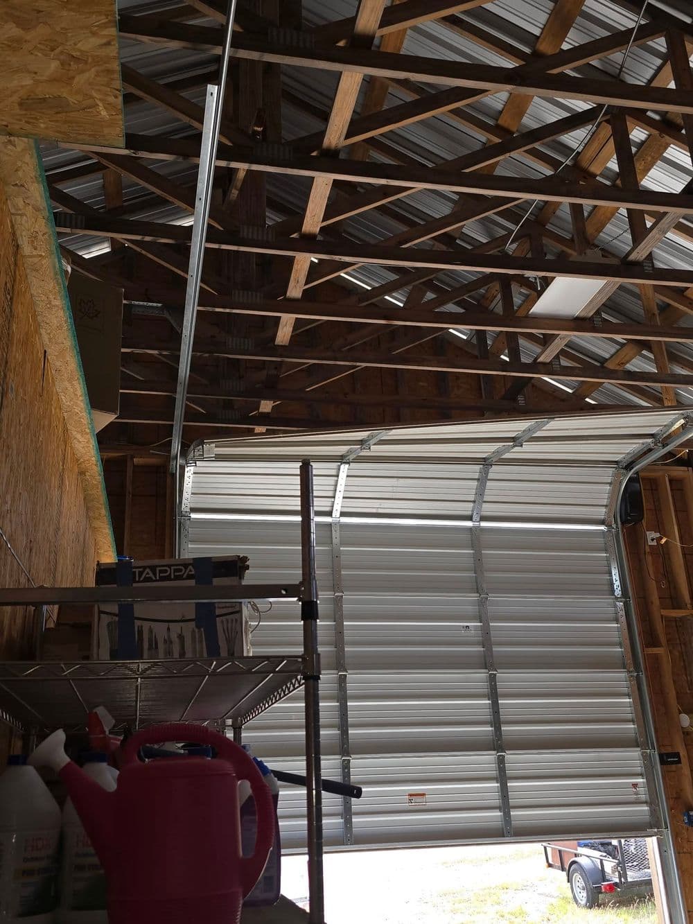 Interior view of a garage showcasing a raised garage door and exposed wooden beams.