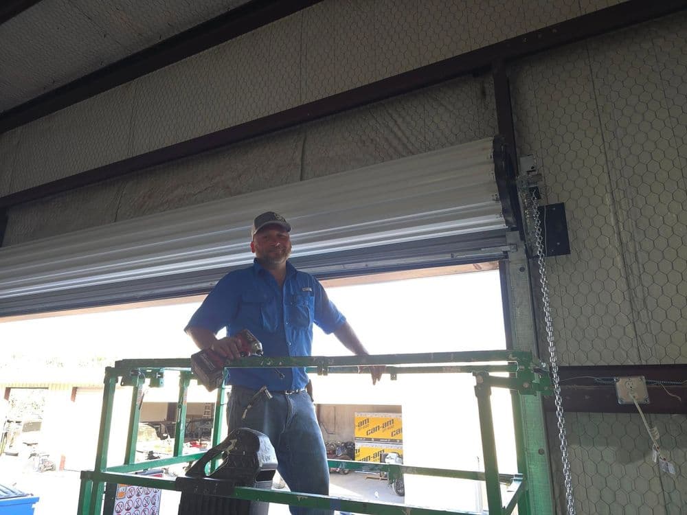 Man in blue shirt operating lift for garage door installation. Industrial setting.