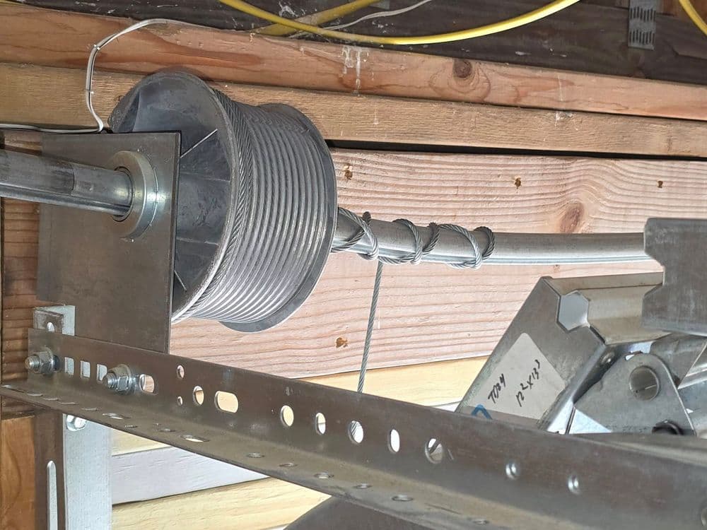 Close-up of a metal spool with wire, mounted on a wooden structure, showing installation details.