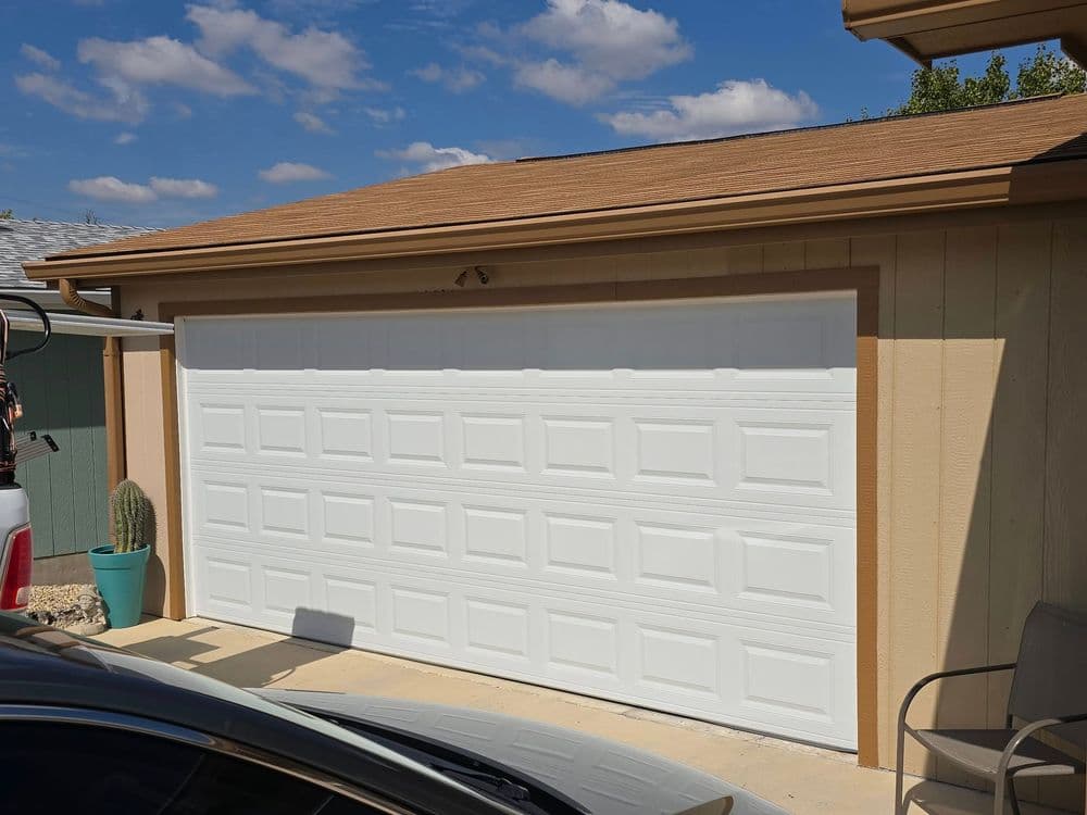 White garage door on a house with a blue sky and clouds, featuring a cactus nearby.